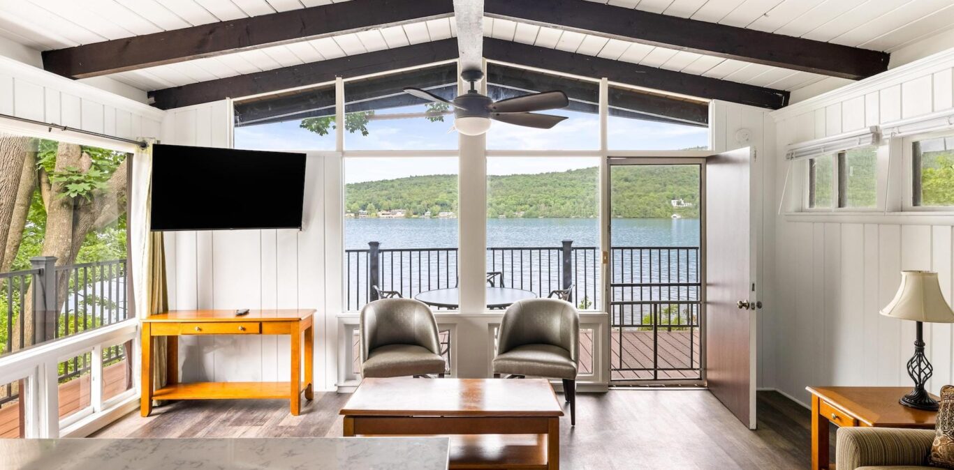A wide-angle view of a living room with a balcony overlooking a lake.