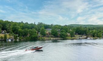 A boat is traveling down Lake George in front of a house.