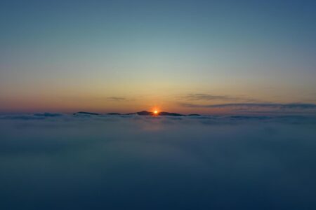 A picturesque sunrise over mountaintops seen from above the clouds