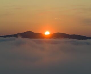 Sun rises over mountains, seen from above the clouds