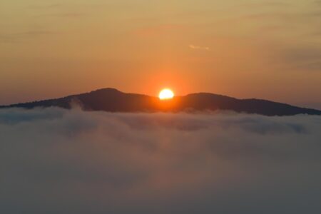 Sun rises over mountains, seen from above the clouds