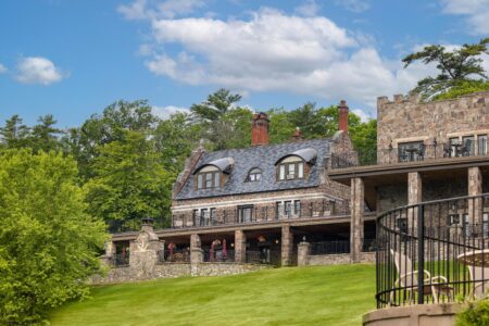 A large stone house sits atop a hill overlooking Lake George.