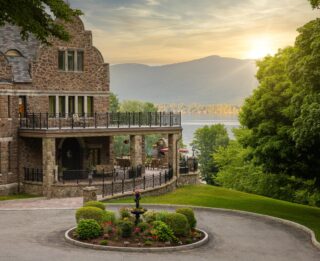 A grand stone house overlooks a lake.