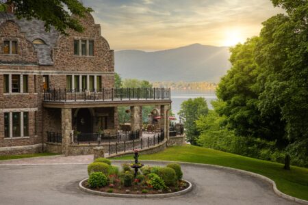 A grand stone house overlooks a lake.