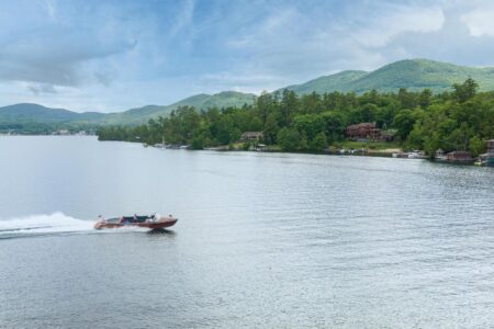 A boat is traveling down a lake with trees in the background, showcasing Lake George lodging.