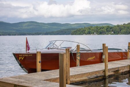 A wooden boat docked at a Lake George dock on a lake.