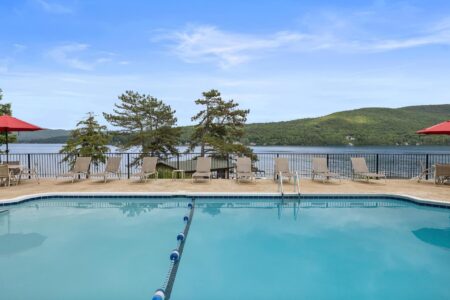 A swimming pool at one of the best hotels in Lake George with lounge chairs and a view of Lake George for a perfect Lake George vacation.