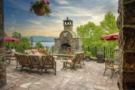 A Lake George resort featuring a patio with furniture and a fireplace overlooking the beautiful lake.