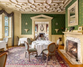 An opulent dining room at The Erlowest, featuring beautiful interiors, tables set for dinner and a fireplace.