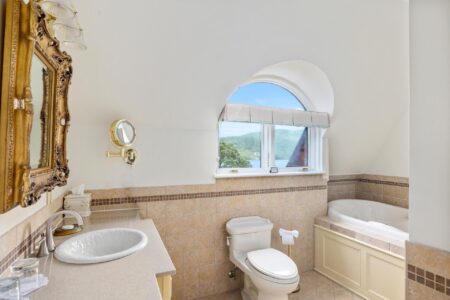 A Lake George resort's bathroom, featuring an arched window and a toilet.