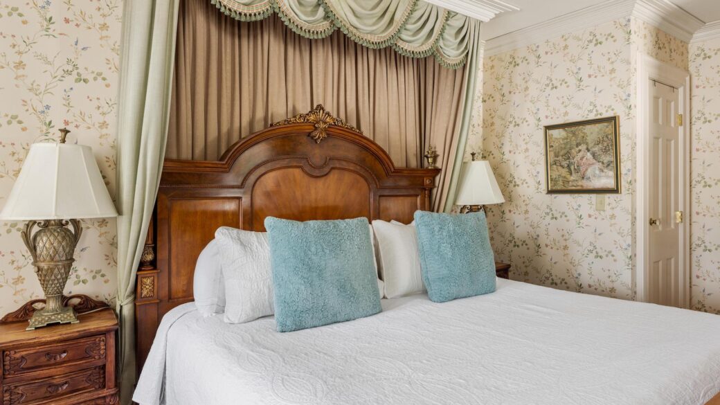 A bed in a Lake George hotel room with floral wallpaper and blue pillows.