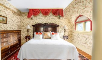 A cozy bed in a bedroom with floral wallpaper at a Lake George vacation retreat.