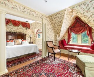 A wide view of a luxurious hotel room with a large bed, window seat, and sitting area.