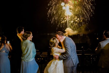A bride and groom share a kiss during their Lake George resort wedding, with fireworks lighting up the sky.