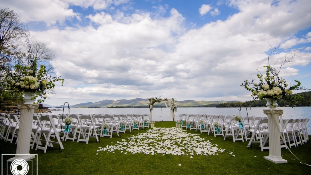 An outdoor wedding ceremony at a Lake George resort, with white chairs and a lake in the background.