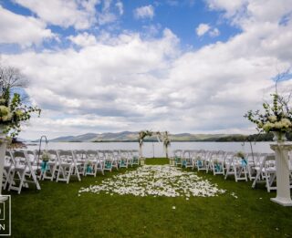 An outdoor wedding ceremony at a Lake George resort, with white chairs and a lake in the background.
