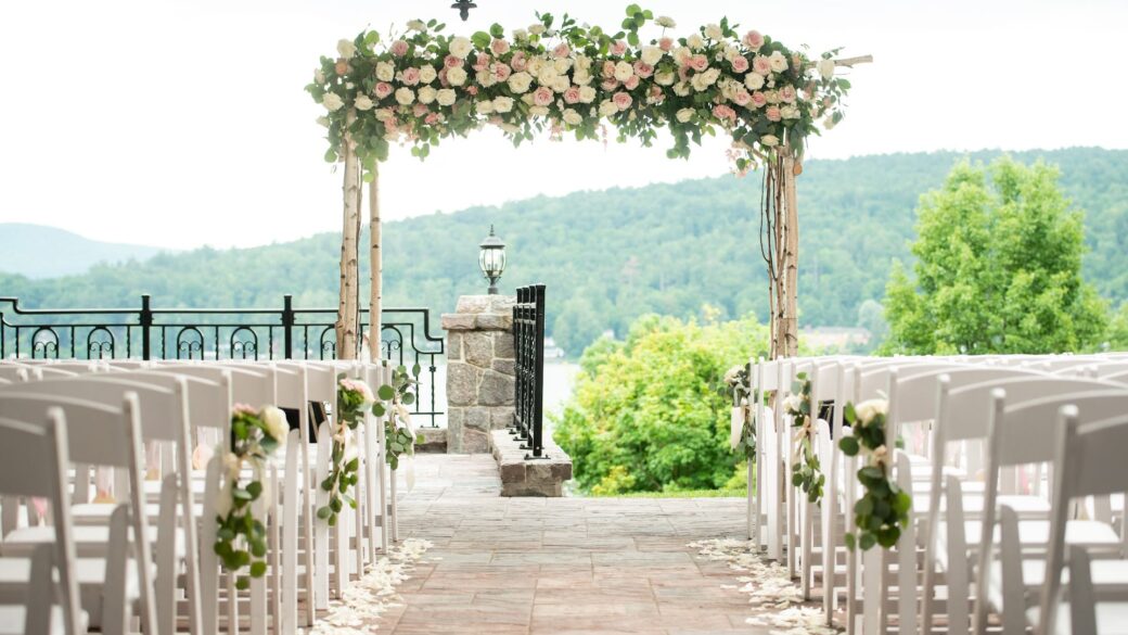 A Lake George wedding ceremony set up with white chairs and flowers at Erlowest, one of the Lake George hotels.