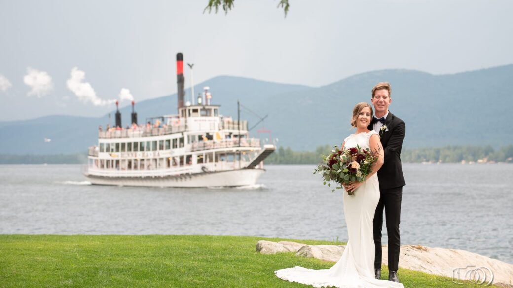 A newlywed couple posing in front of a boat on Lake George.