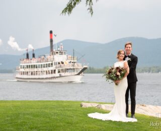 A newlywed couple posing in front of a boat on Lake George.