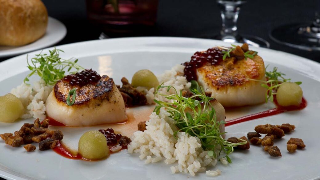 Scallops on a plate with rice and grapes.