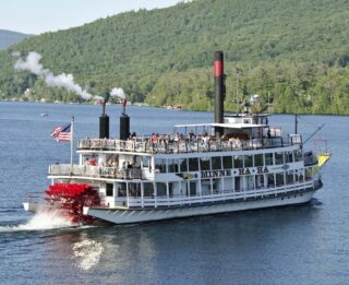 A steamboat traveling down a lake with mountains in the background.