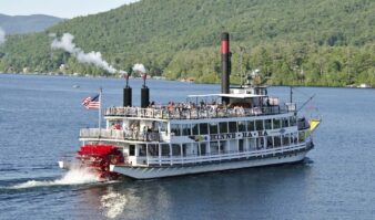 A steamboat traveling down a lake with mountains in the background.