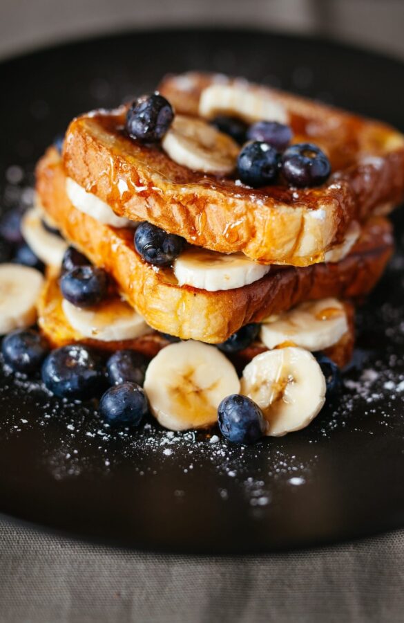 A plate of french toast topped with bananas and blueberries.