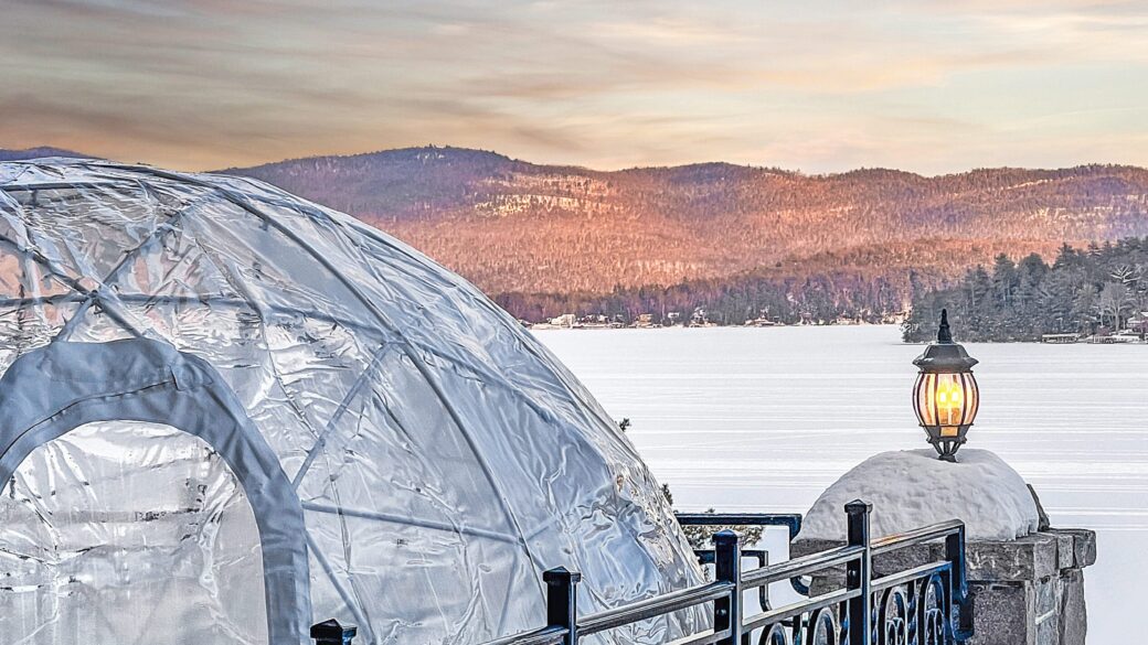 A glass igloo sitting on the edge of a lake.