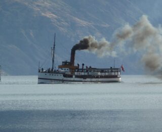 A Lake George steamboat sails along the mountainside waters, puffing out clouds of steam.