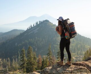 A woman with a backpack standing on top of a mountain.