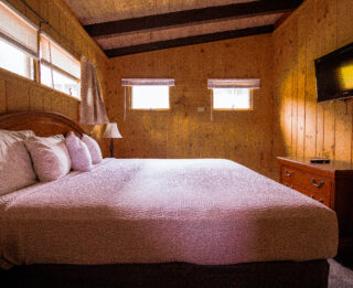 A wide view of a cozy room with a large bed, wood paneling, and a TV on the wall.
