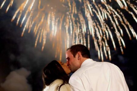 A bride and groom kiss in front of a firework display.