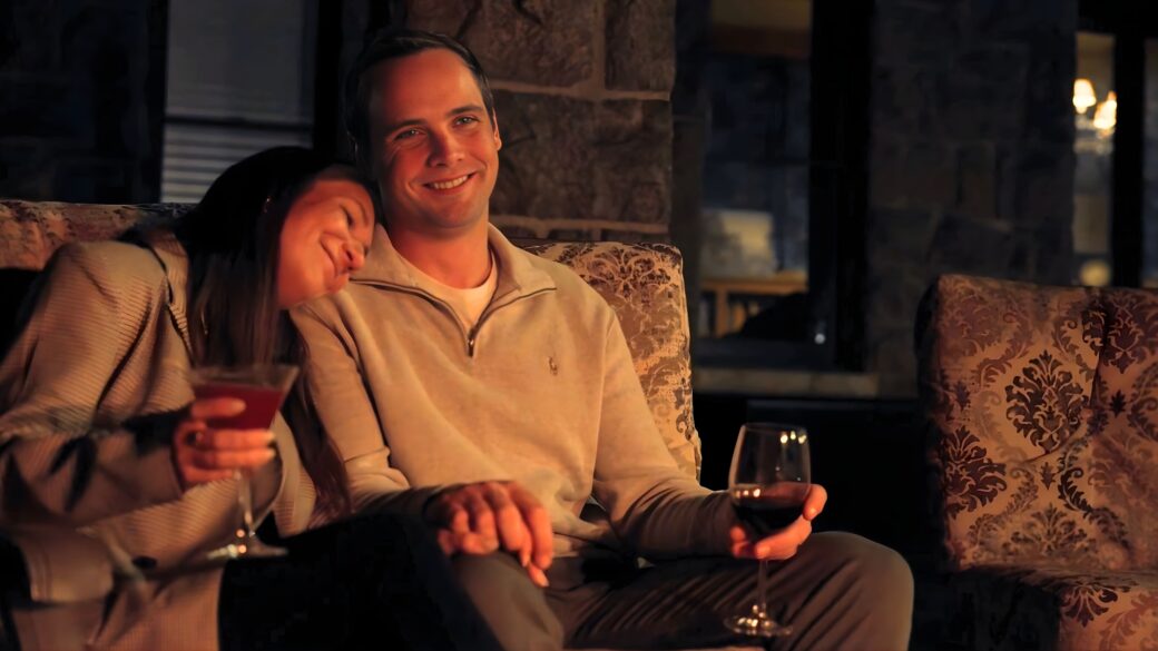 Couple enjoying wine by an outdoor fireplace, seated on couches at The Inn at Erlowest