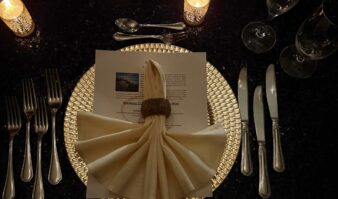 Fancy table setting with high-end silverware and glassware, a decorated Napkin on top of a golden plate, glittery table cloth and lit candles
