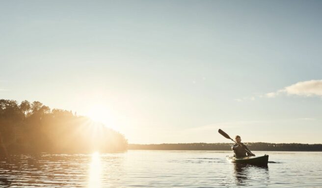 Man in a row boat rows across a tranquil lake under a clear sunset sky